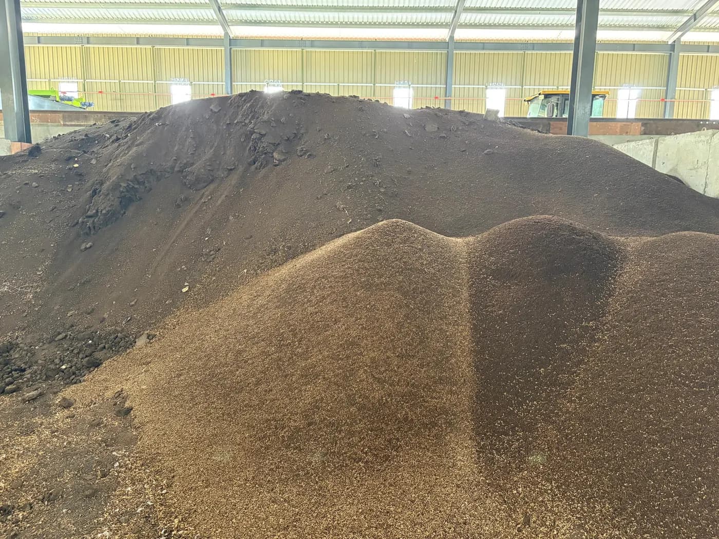 Mounds of dark frass inside the cultivation shed, with a yellow loader visible behind